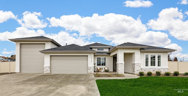 prairie-style house with a front lawn, stone siding, fence, concrete driveway, and an attached garage