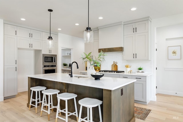 kitchen with light wood finished floors, a sink, light countertops, custom range hood, and appliances with stainless steel finishes