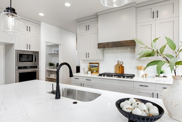 kitchen with light stone countertops, a sink, decorative backsplash, stainless steel appliances, and custom range hood