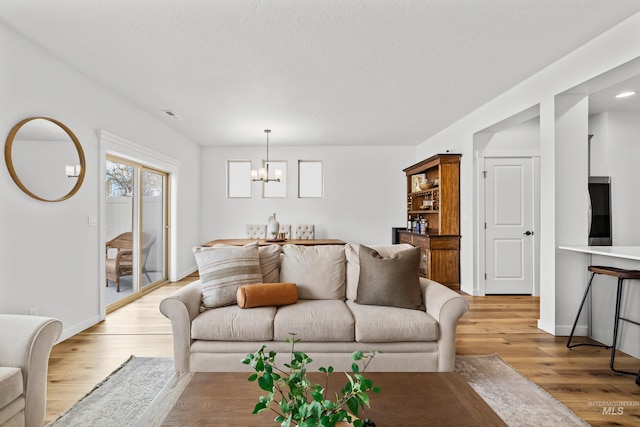 living room with an inviting chandelier, visible vents, baseboards, and light wood finished floors