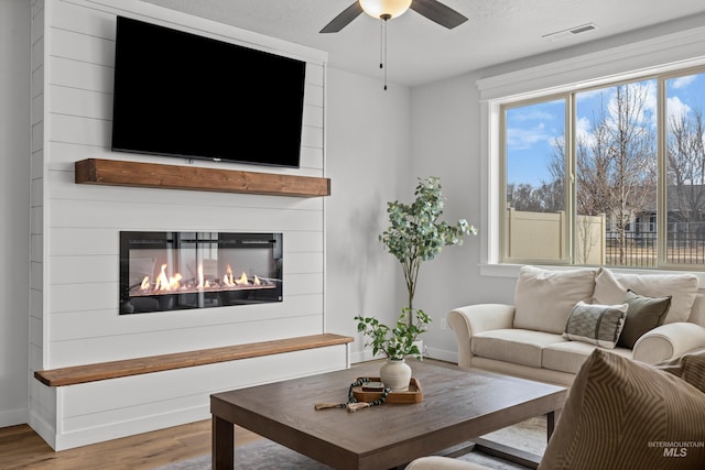 living room featuring wood finished floors, baseboards, visible vents, a fireplace, and ceiling fan