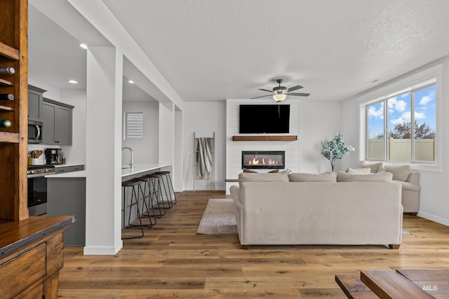 living area with a ceiling fan, a textured ceiling, a fireplace, light wood finished floors, and baseboards