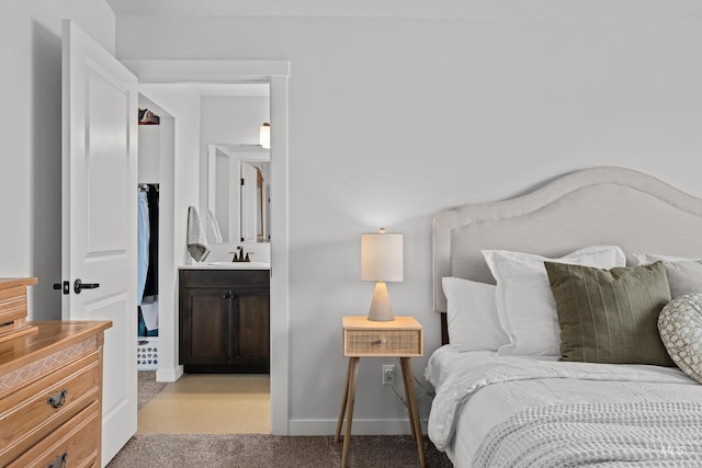 bedroom featuring ensuite bath, light carpet, baseboards, and a sink