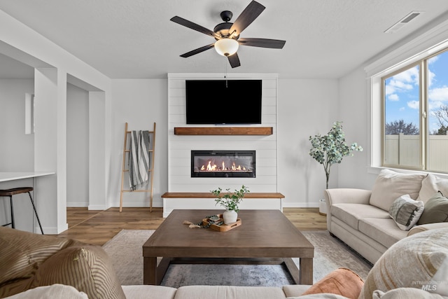 living area featuring visible vents, a fireplace, baseboards, and wood finished floors