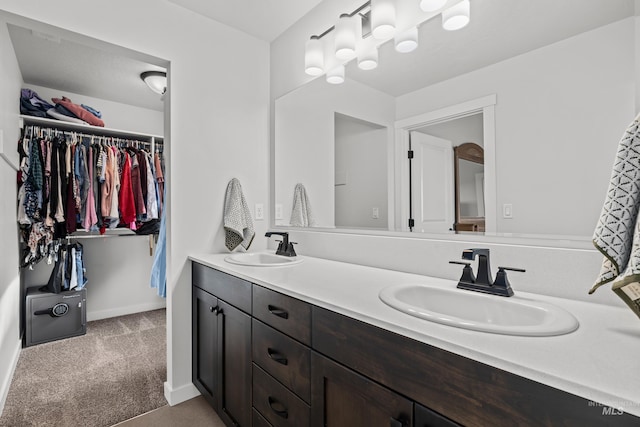 full bath featuring double vanity, a walk in closet, baseboards, and a sink