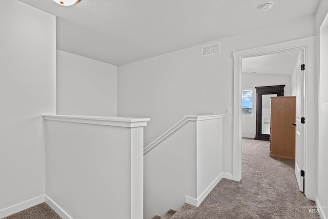 corridor featuring an upstairs landing, visible vents, baseboards, and carpet