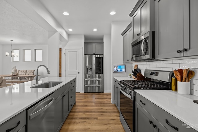 kitchen with light wood finished floors, appliances with stainless steel finishes, light countertops, and a sink