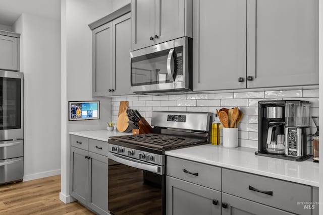 kitchen featuring decorative backsplash, light wood-type flooring, gray cabinets, and stainless steel appliances