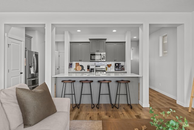 kitchen with gray cabinetry, decorative backsplash, a kitchen breakfast bar, appliances with stainless steel finishes, and a sink