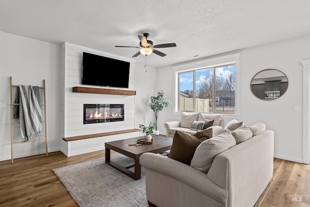 living room with visible vents, a large fireplace, baseboards, wood finished floors, and a textured ceiling