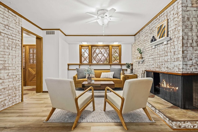 living room with light hardwood / wood-style flooring, brick wall, a brick fireplace, crown molding, and ceiling fan