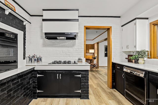 kitchen featuring white cabinetry, brick wall, light hardwood / wood-style flooring, range hood, and black appliances