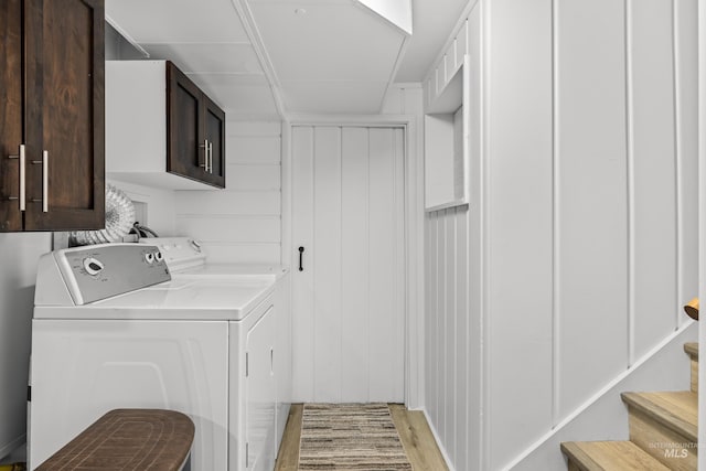 washroom featuring cabinets, washing machine and clothes dryer, and light hardwood / wood-style flooring