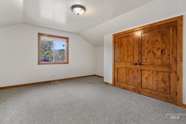 bonus room featuring lofted ceiling, carpet flooring, a textured ceiling, and baseboards