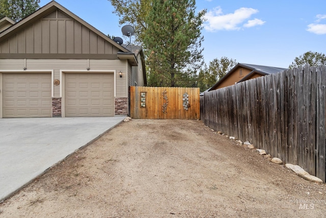 exterior space with an attached garage, fence, stone siding, driveway, and board and batten siding