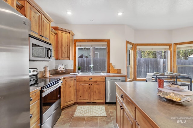 kitchen with light tile patterned floors, brown cabinetry, appliances with stainless steel finishes, a sink, and recessed lighting