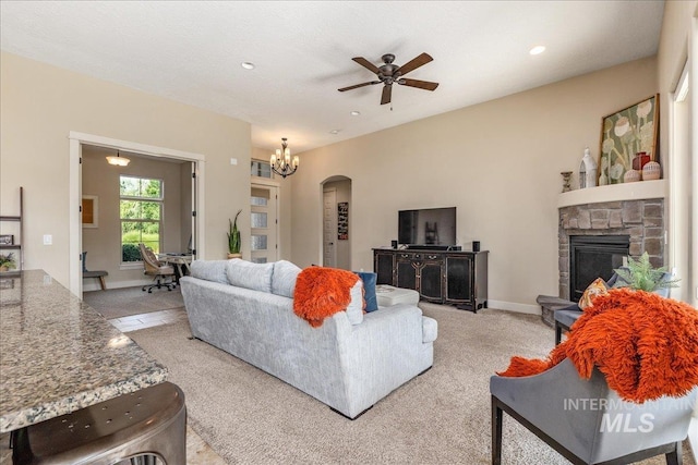 living room featuring ceiling fan with notable chandelier, a stone fireplace, and light colored carpet