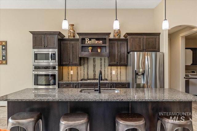 kitchen with stainless steel appliances, dark stone countertops, dark brown cabinetry, and decorative light fixtures