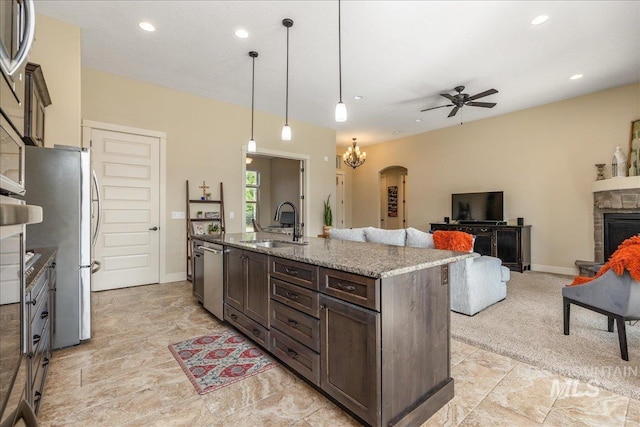 kitchen featuring sink, light stone counters, decorative light fixtures, a center island with sink, and a fireplace