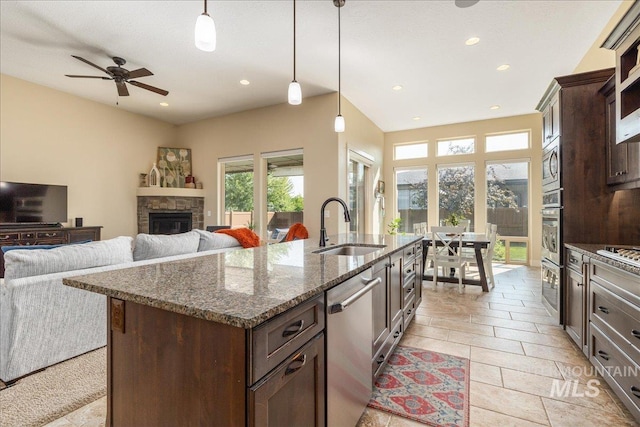 kitchen with sink, decorative light fixtures, dark stone countertops, stainless steel appliances, and a kitchen island with sink