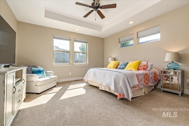 bedroom with light colored carpet, a raised ceiling, and ceiling fan