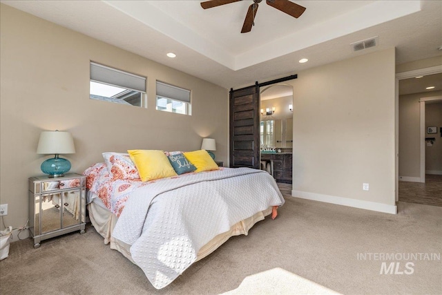 bedroom with a barn door, light colored carpet, ensuite bath, and a tray ceiling