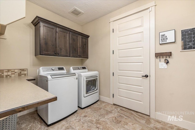 clothes washing area featuring cabinets, washing machine and clothes dryer, and a textured ceiling