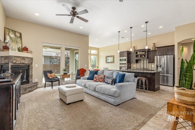 living room with ceiling fan, a stone fireplace, sink, and a textured ceiling