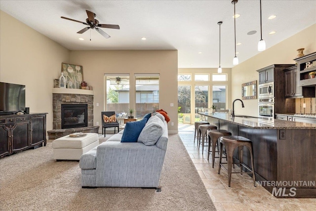 living room with a stone fireplace, sink, and ceiling fan