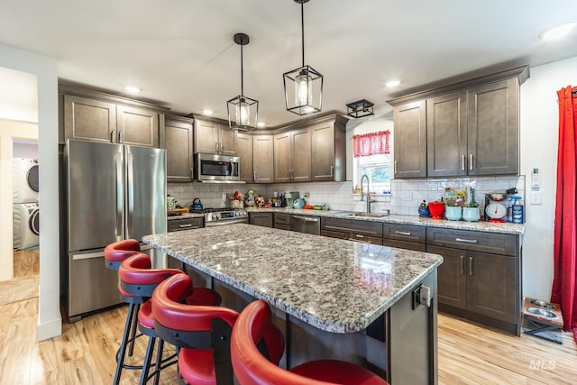 kitchen with light wood-type flooring, sink, a kitchen island, stainless steel appliances, and decorative light fixtures