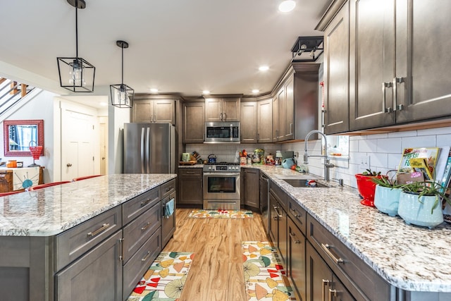 kitchen featuring light stone countertops, stainless steel appliances, light hardwood / wood-style floors, and decorative light fixtures