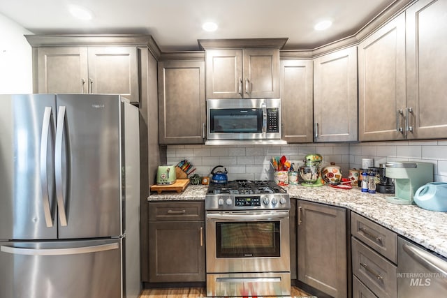 kitchen with light stone countertops, appliances with stainless steel finishes, light hardwood / wood-style floors, and decorative backsplash