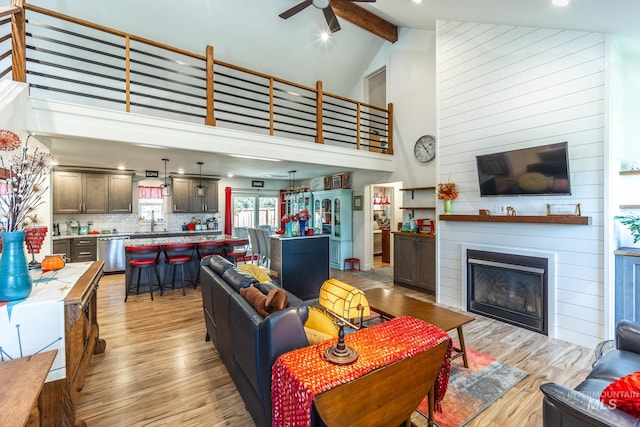 living room featuring ceiling fan, beam ceiling, wooden walls, high vaulted ceiling, and light wood-type flooring