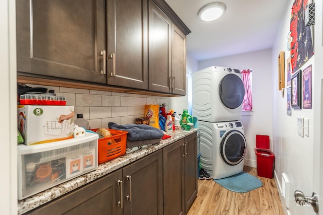 washroom with stacked washer and clothes dryer, light hardwood / wood-style flooring, and cabinets