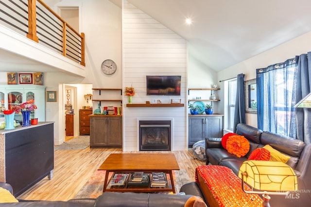 living room featuring light hardwood / wood-style flooring, a large fireplace, and high vaulted ceiling