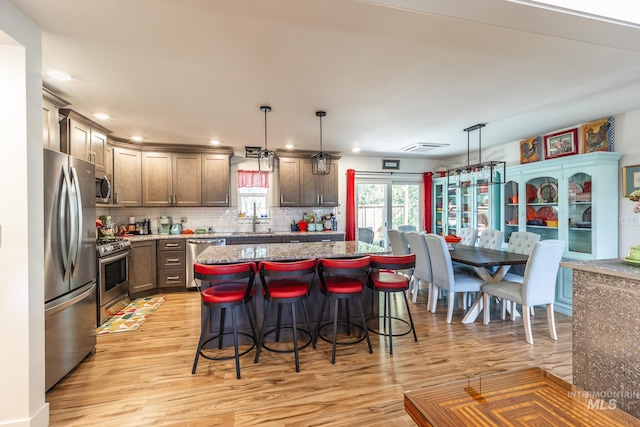 kitchen with appliances with stainless steel finishes, a kitchen breakfast bar, light hardwood / wood-style floors, pendant lighting, and a center island