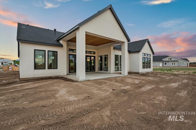 rear view of property featuring a patio, a shingled roof, and stucco siding