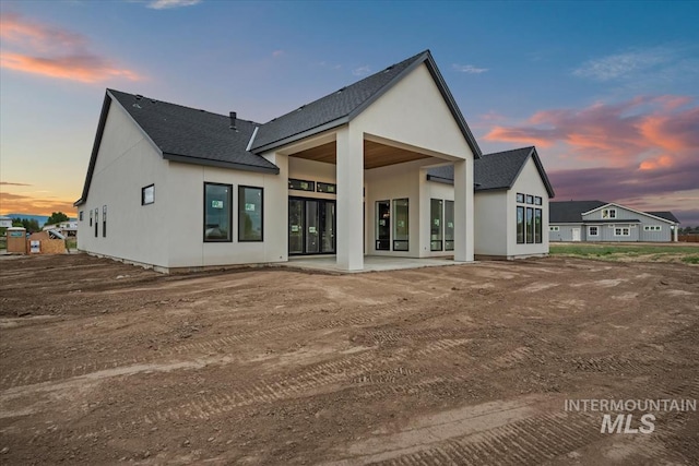 back of property at dusk featuring a patio area, roof with shingles, and stucco siding