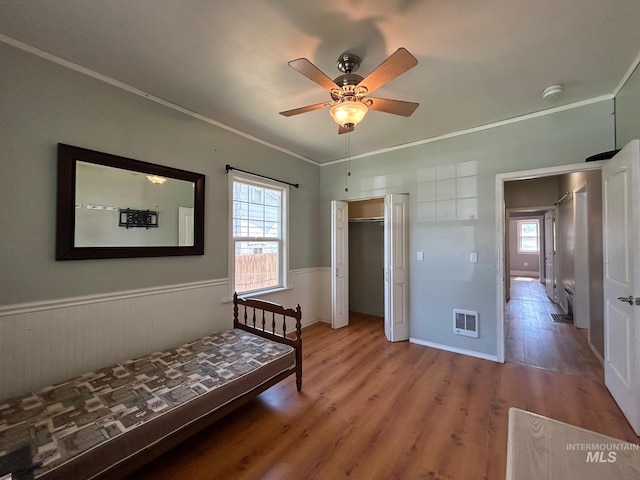 bedroom with a closet, hardwood / wood-style flooring, ceiling fan, and crown molding