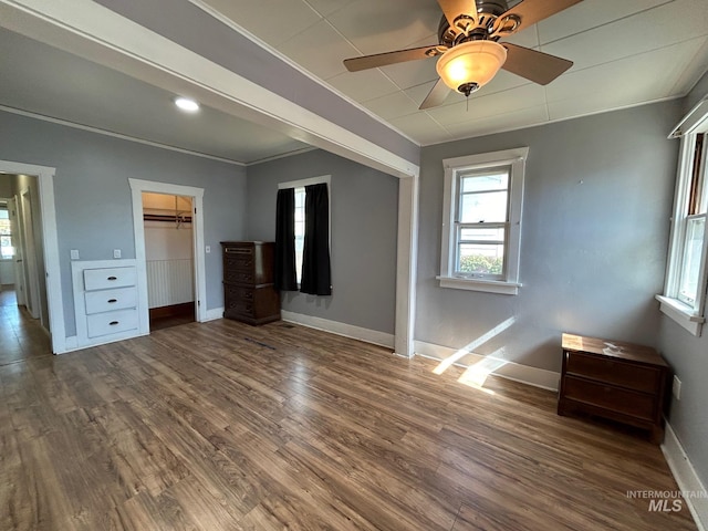 unfurnished bedroom with a walk in closet, ceiling fan, crown molding, dark wood-type flooring, and a closet