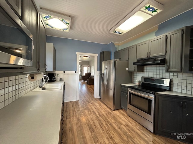 kitchen with gray cabinetry, sink, light wood-type flooring, appliances with stainless steel finishes, and tasteful backsplash