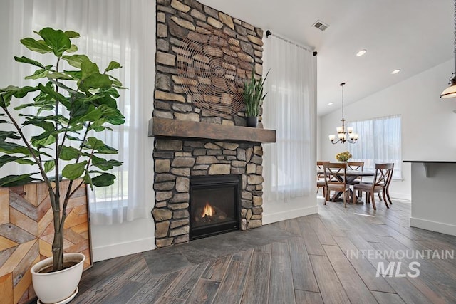 living room featuring dark wood-type flooring, a stone fireplace, a healthy amount of sunlight, and vaulted ceiling