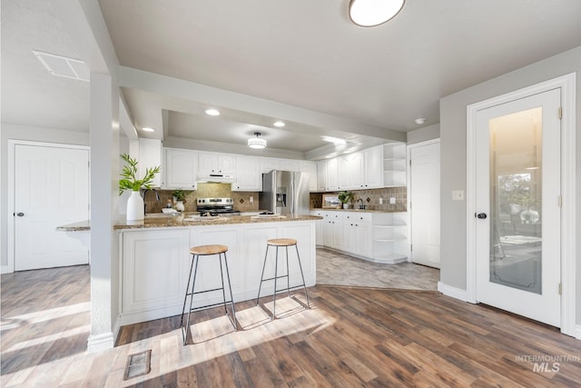 kitchen with kitchen peninsula, light stone countertops, stainless steel appliances, backsplash, and white cabinetry