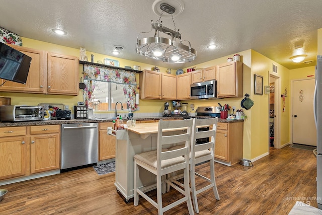 kitchen featuring stainless steel appliances, light brown cabinetry, hardwood / wood-style floors, and a textured ceiling