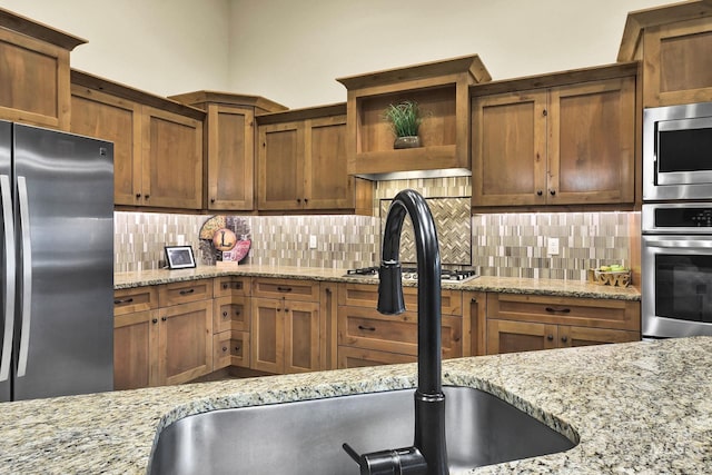 kitchen with stainless steel appliances, a sink, tasteful backsplash, and light stone countertops