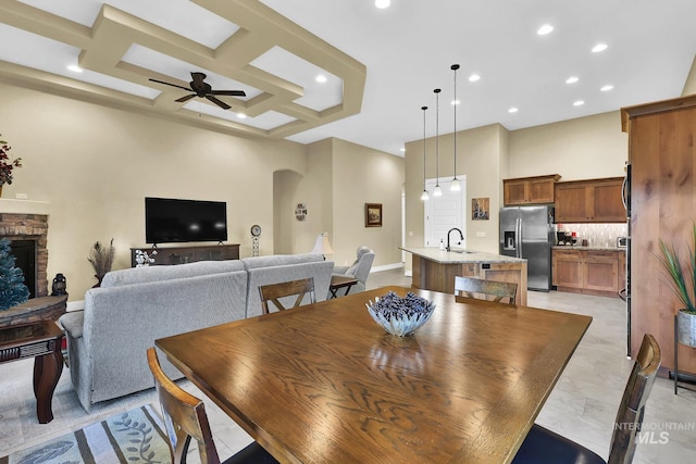 dining area featuring recessed lighting, arched walkways, ceiling fan, a stone fireplace, and coffered ceiling