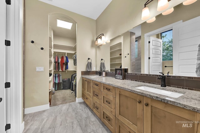 full bathroom featuring baseboards, double vanity, a walk in closet, and marble look tile flooring