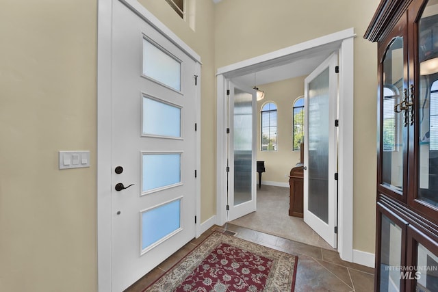 foyer entrance with baseboards, dark tile patterned floors, and french doors