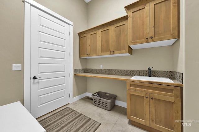 kitchen featuring a sink, light marble finish flooring, light countertops, baseboards, and brown cabinetry