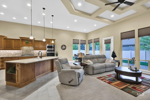 living room with plenty of natural light, ceiling fan, a high ceiling, recessed lighting, and coffered ceiling